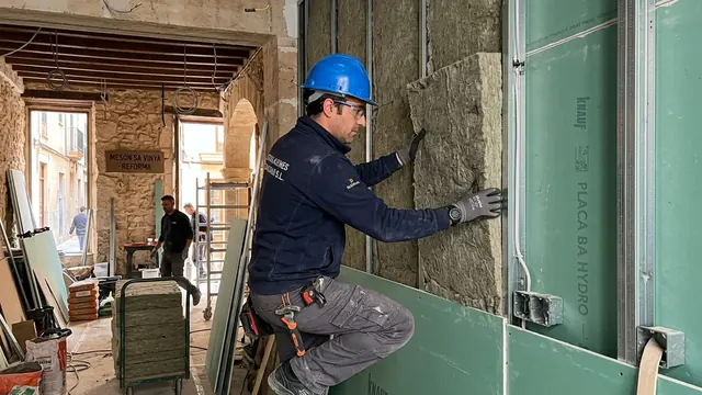 Operario colocando lana mineral en un trasdosado acústico con placa de yeso laminado
