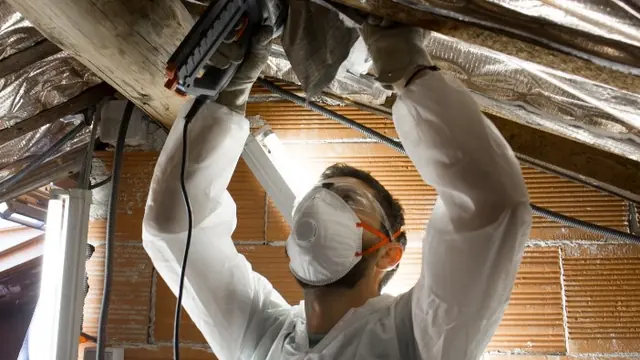 Operario con mascarilla fijando con grapadora un aislante reflexivo bajo la cubierta