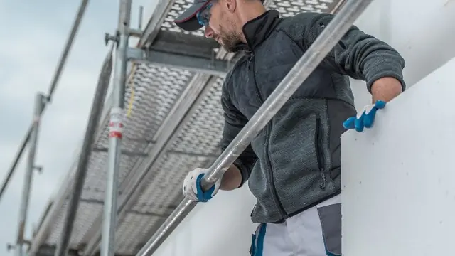 Operario con guantes sujetando un panel aislante en un andamio de fachada